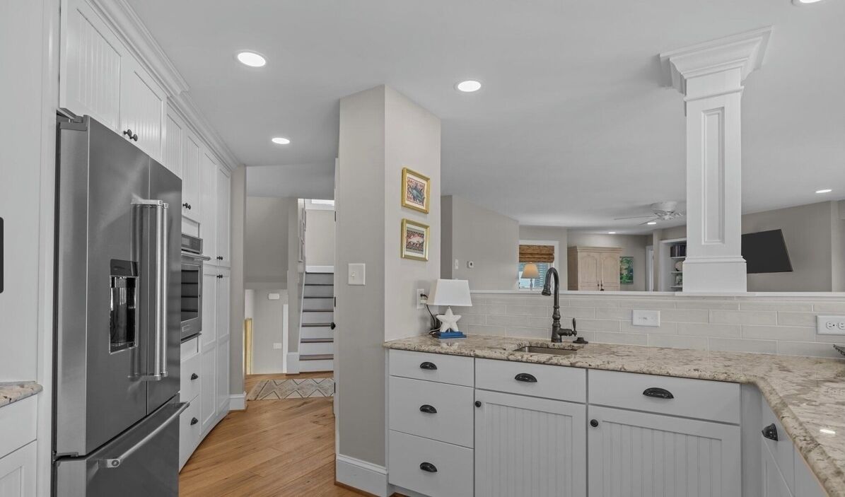 A modern kitchen with white cabinetry, a stainless steel refrigerator, and a granite countertop.