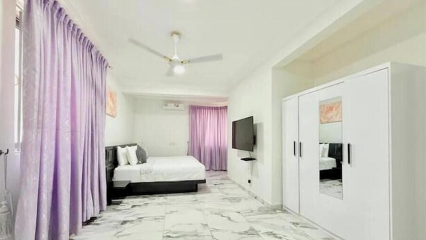 A hotel room with a bed, a wardrobe, a ceiling fan, and a TV. - Classic 2-Bedroom house in East Legon

Share

Save (Accra)