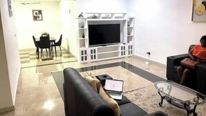A living room with a sofa, a glass coffee table, a TV, and a dining area with a table and chairs. - Classic 2-Bedroom house in East Legon

Share

Save (Accra)