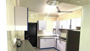 A kitchen with white cabinets, a black backsplash, a stainless steel sink, and a ceiling fan. - Classic 2-Bedroom house in East Legon

Share

Save (Accra)
