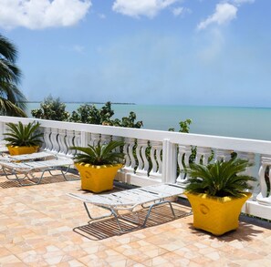 A balcony with white railings, yellow planters with green plants, and white lounge chairs.