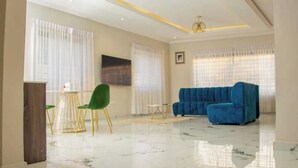A spacious living room with a blue sofa, green chairs, and a marble floor.