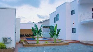 A courtyard with a swimming pool, surrounded by white buildings, and includes a small garden area with plants.