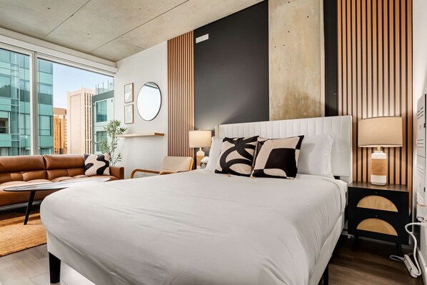 Ein modernes Hotelzimmer mit einem großen Bett, einer Couch, einem runden Spiegel und Blick auf die Stadt.