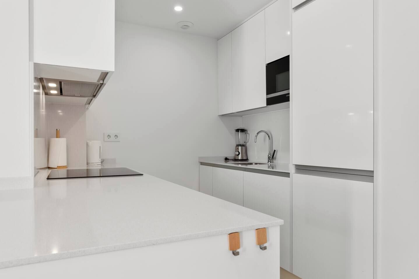 Una cocina moderna con armarios blancos, un microondas integrado y un lavamanos de acero inoxidable.