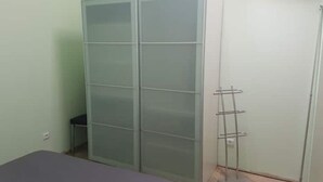 Ein Zimmer mit einem Bett, einem hohen Kleiderschrank und einem Metallregal.