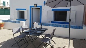 Ein Essbereich im Freien mit einem Tisch für zwei Personen, einem Sonnenschirm und einem Gebäude mit blauen Verzierungen und Fenstern.