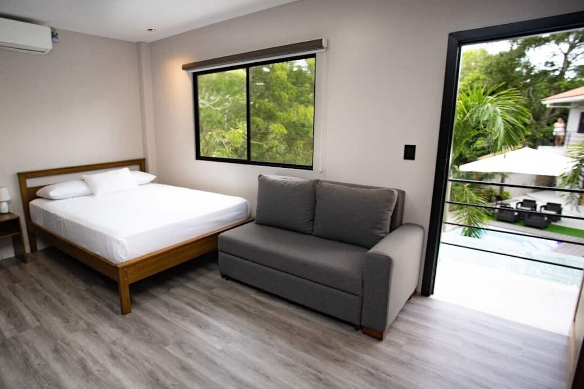 Ein Schlafzimmer mit einem Bett, einem Nachttisch, einer Couch, einem Fenster und Blick ins Freie.