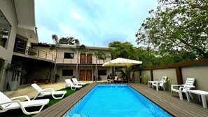 A swimming pool with lounge chairs and umbrellas, surrounded by a two-story building with balconies and potted plants. - OCEAN DRIVE LODGE MONTAÑITA (Montañita)