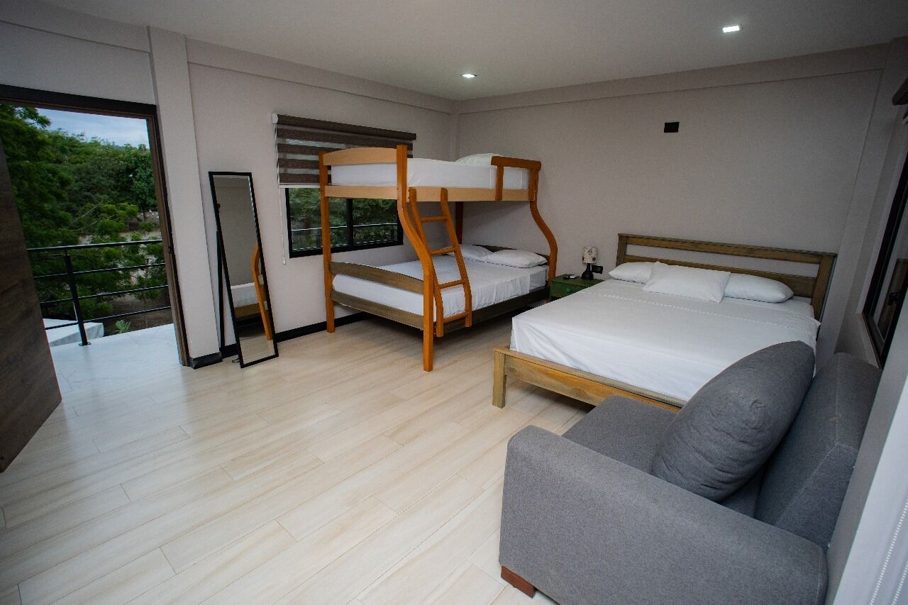 A bedroom with a bunk bed, a single bed, a sofa, and a balcony with a view of greenery.