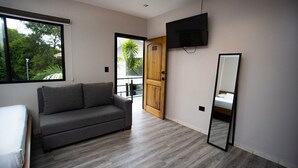 Une pièce moderne avec un canapé gris, une porte en bois, un téléviseur fixé au mur et une grande fenêtre.