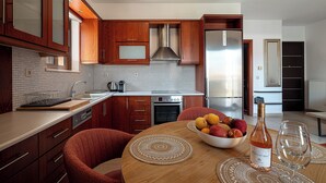 A modern kitchen with wooden cabinets, a stainless steel refrigerator, and a dining table with a fruit bowl and wine glass. - Modern flat in Chania, Crete - 5 min from the beach, 10 min from the old town! (Chania)