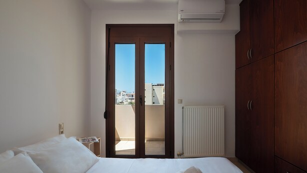 A hotel room with a bed, a wooden wardrobe, a radiator, and a window with a view of buildings. - Modern flat in Chania, Crete - 5 min from the beach, 10 min from the old town! (Chania)