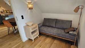 Un espacio habitable pequeño con un sofá, una mesita de madera, una lámpara de pie y una silla.