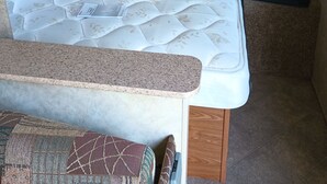 A compact RV interior with a bed, kitchenette, and wooden cabinets.