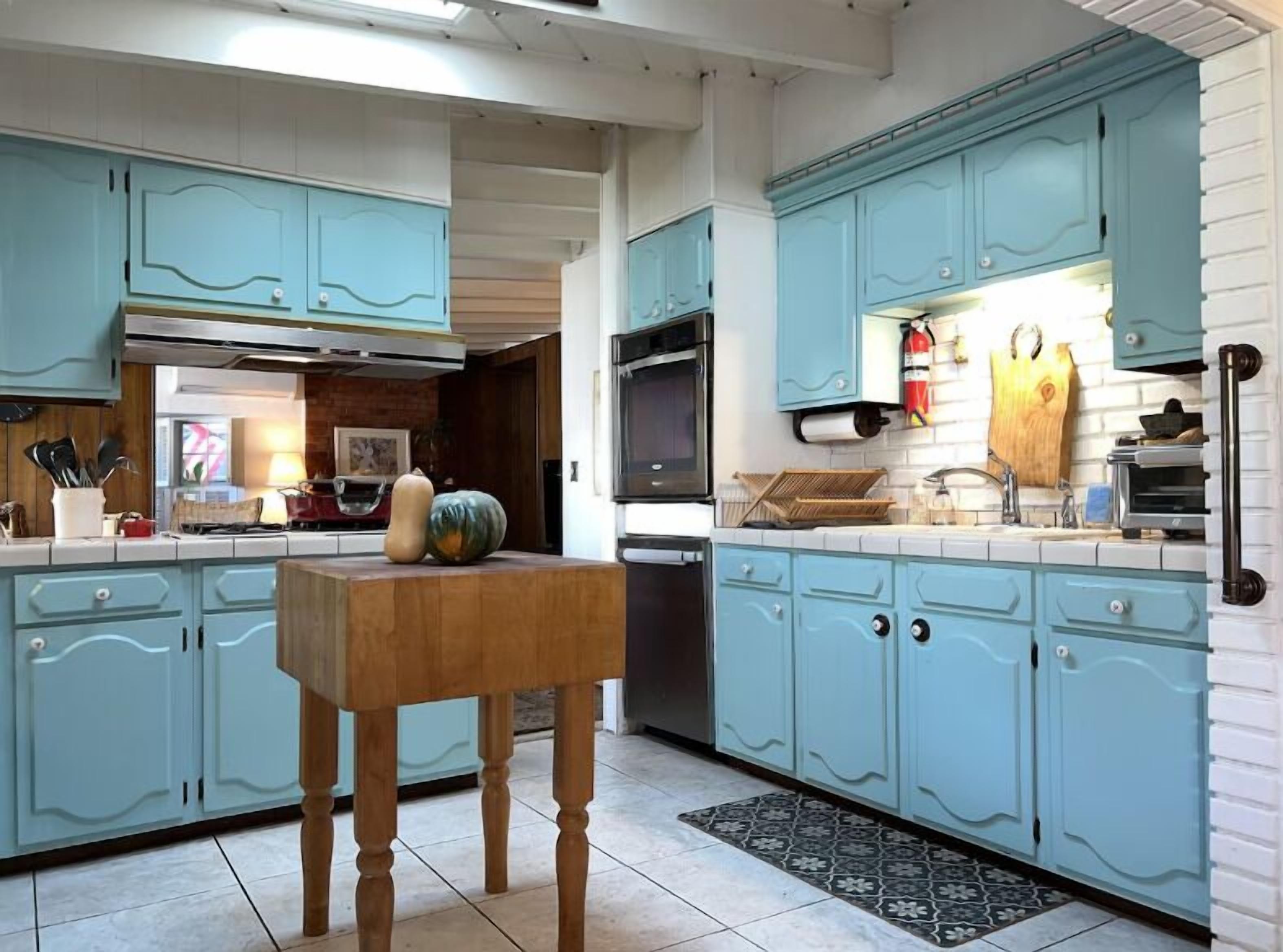 A kitchen with light blue cabinets, a wooden table, and a tiled floor.