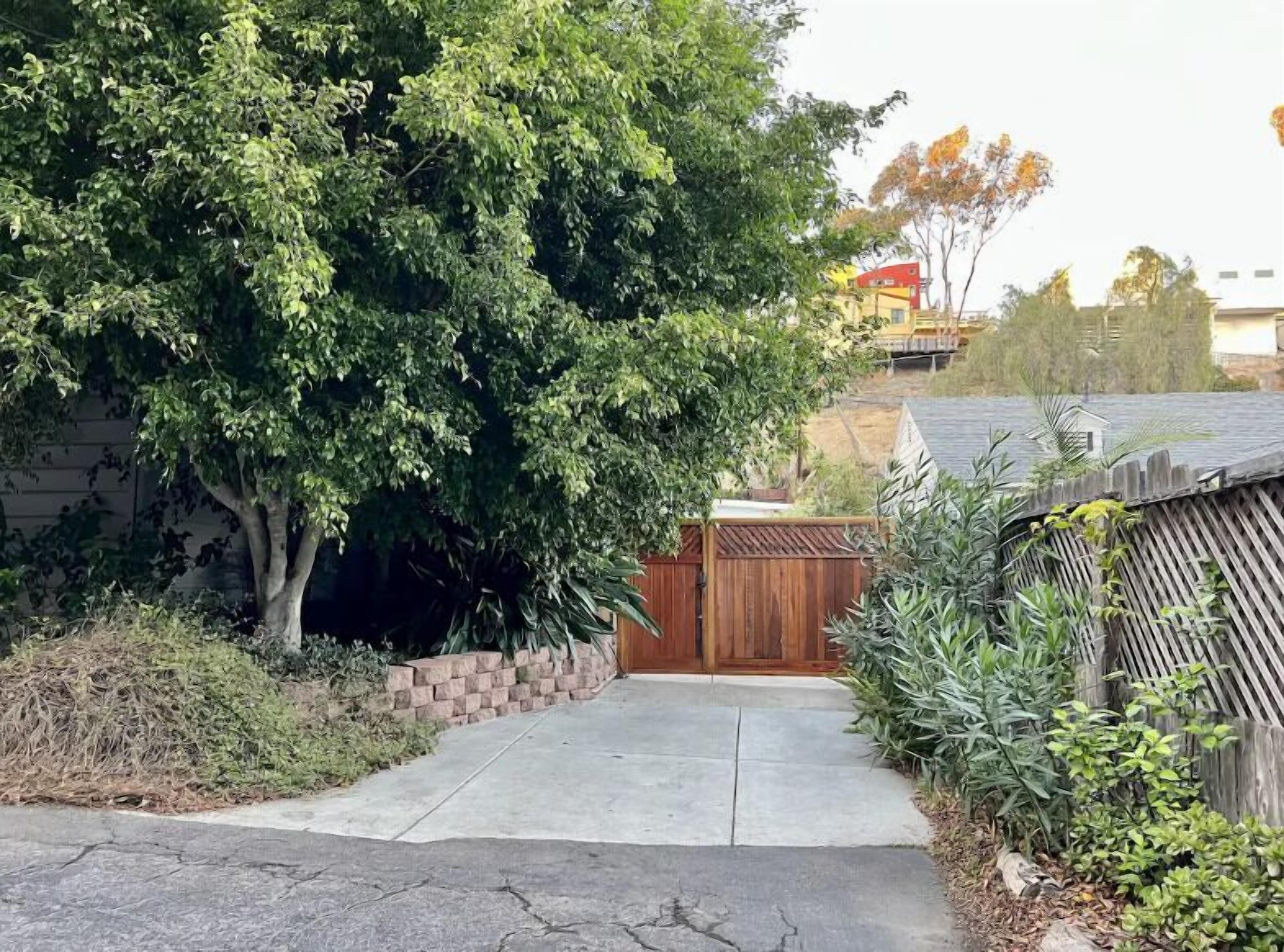 A residential driveway with a wooden gate, a tree, and a brick wall.