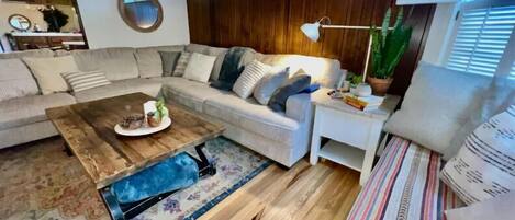 A modern living room with a sectional sofa, a wooden coffee table, a striped rug, and a small side table with a lamp and a plant.