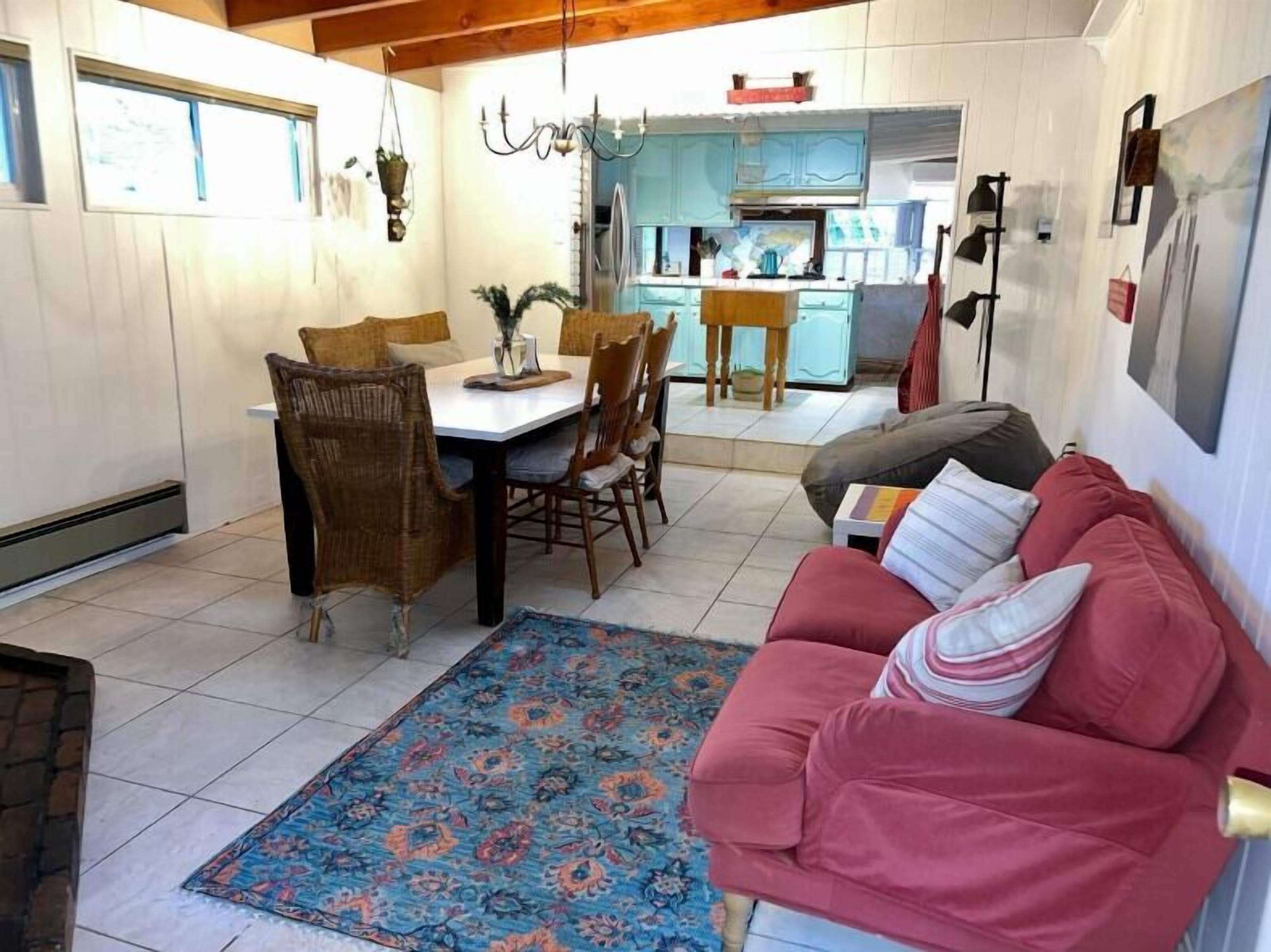 Ein gemütliches Wohnzimmer mit einem roten Sofa, einem Esstisch mit Stühlen und einer Küchenzeile im Hintergrund.