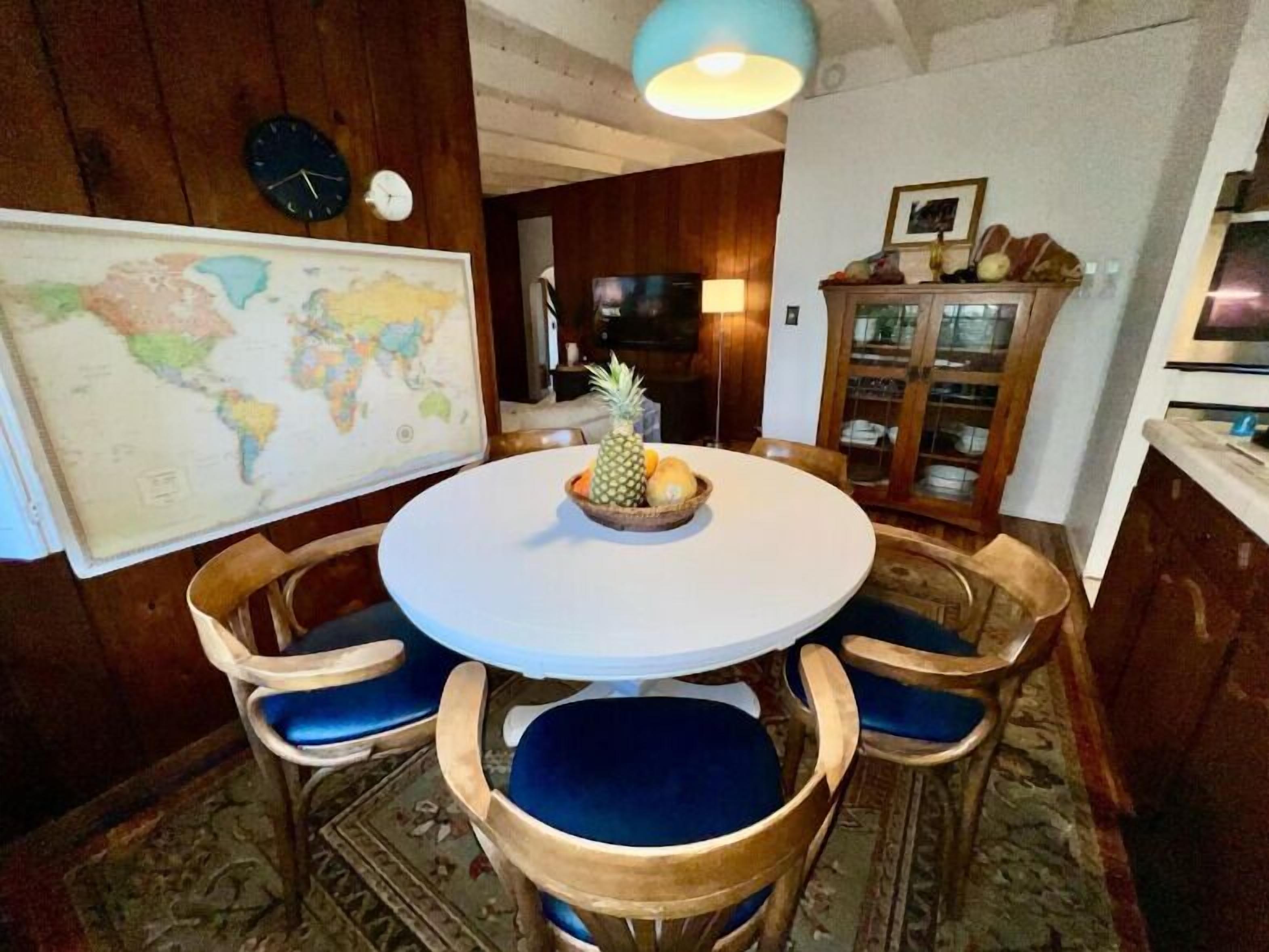A round dining table with a world map, wooden chairs, and a pineapple centerpiece.