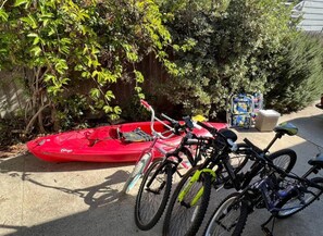 A red kayak and two bicycles parked on a concrete surface, with a wooden fence and greenery in the background. - New Cozy Studio 2 Queen Beds, Kitchen Walk to Water (San Diego)
