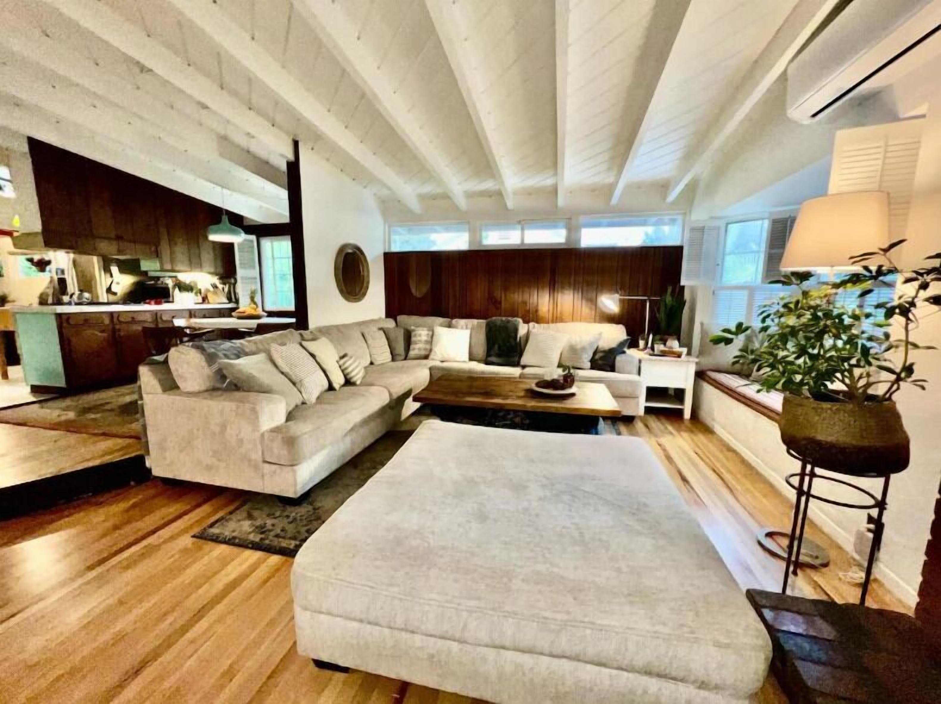 A modern living room with a sectional sofa, a coffee table, and a large ottoman. There is a kitchen area visible in the background.