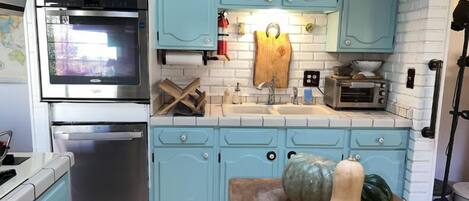 A kitchen with light blue cabinets, a stainless steel oven, a sink, and a wooden table with vegetables.