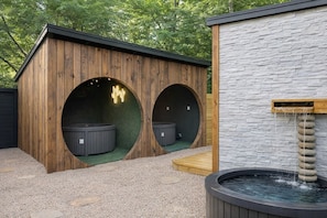 A spa area with two hot tubs, a wooden structure, and a stone wall.