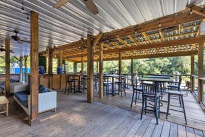 Una terrazza esterna con tavoli e sedie in legno, un'area salotto coperta e vista su piante.