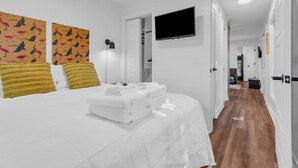 A hotel room with a bed, a television mounted on the wall, and a hallway leading to other rooms.