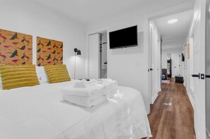 Una camera d'albergo con un letto, una televisione a parete e un corridoio che dà su altre stanze.