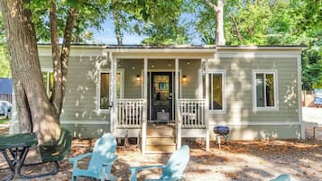 A small, single-story house with a porch, a front door, and a small table and chairs outside.