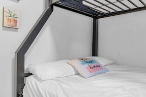 A bunk bed with a metal frame, white bedding, and a pillow with a colorful design.