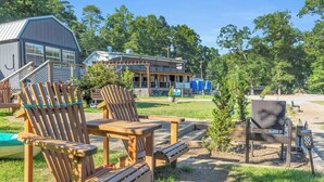 A campground with wooden chairs and tables, a building with a porch, and a small tree.