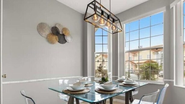 A dining area with a glass table and chairs, a chandelier, and decorative wall art. - Discover " a spacious 3-bedroom house  Enjoy a pool in the condo, fitness room, (Kissimmee)