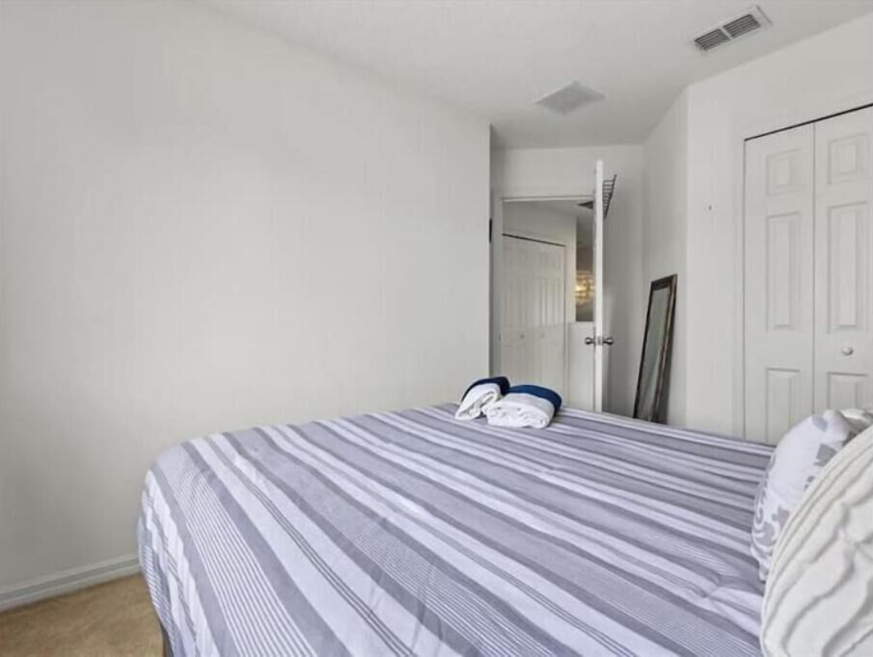 A single bed with a striped bedspread, a door, and a mirror on the wall.