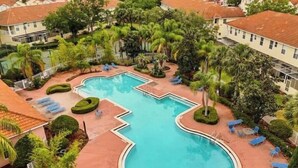 A swimming pool surrounded by palm trees and lounge chairs, with a view of residential buildings in the background. - Discover " a spacious 3-bedroom house  Enjoy a pool in the condo, fitness room, (Kissimmee)