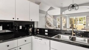 A modern kitchen with white cabinets, black countertops, and stainless steel appliances. - Discover " a spacious 3-bedroom house  Enjoy a pool in the condo, fitness room, (Kissimmee)