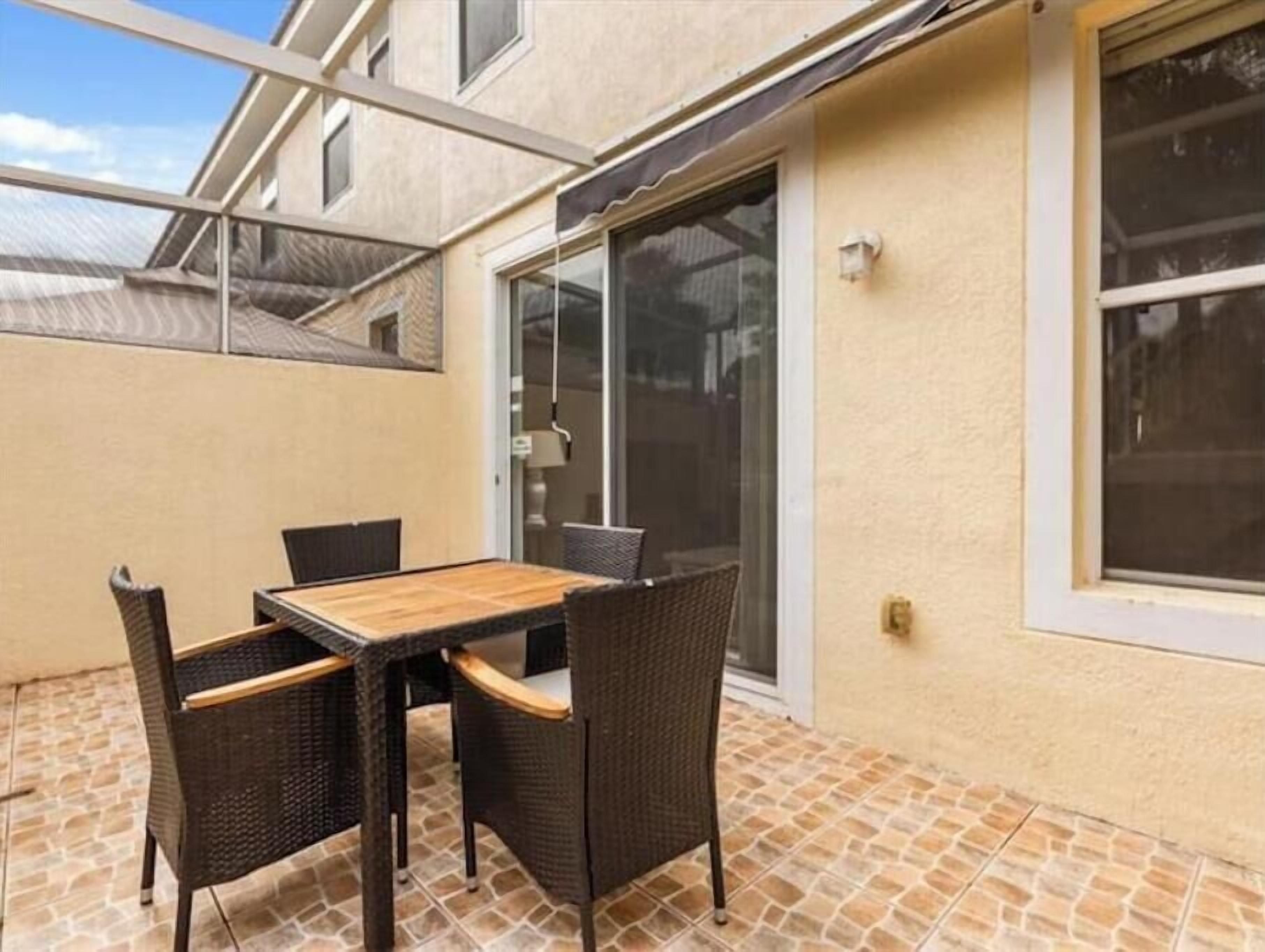 Une terrasse avec une table en bois et quatre chaises en osier, une porte-fenêtre coulissante et un sol carrelé.