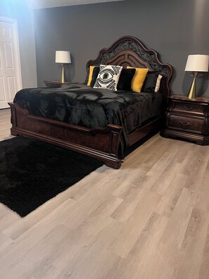 A bedroom with a dark wood bed, two bedside tables with lamps, a black rug, and a grey wall. - Charming house perfectly located in Central City near most popular venues. (New Orleans)