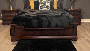A bedroom with a dark wood bed, two nightstands, a black rug, and a chandelier.