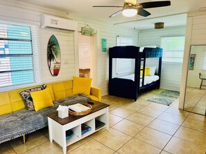 A room with a yellow sofa, a white coffee table, a bunk bed, and a ceiling fan.