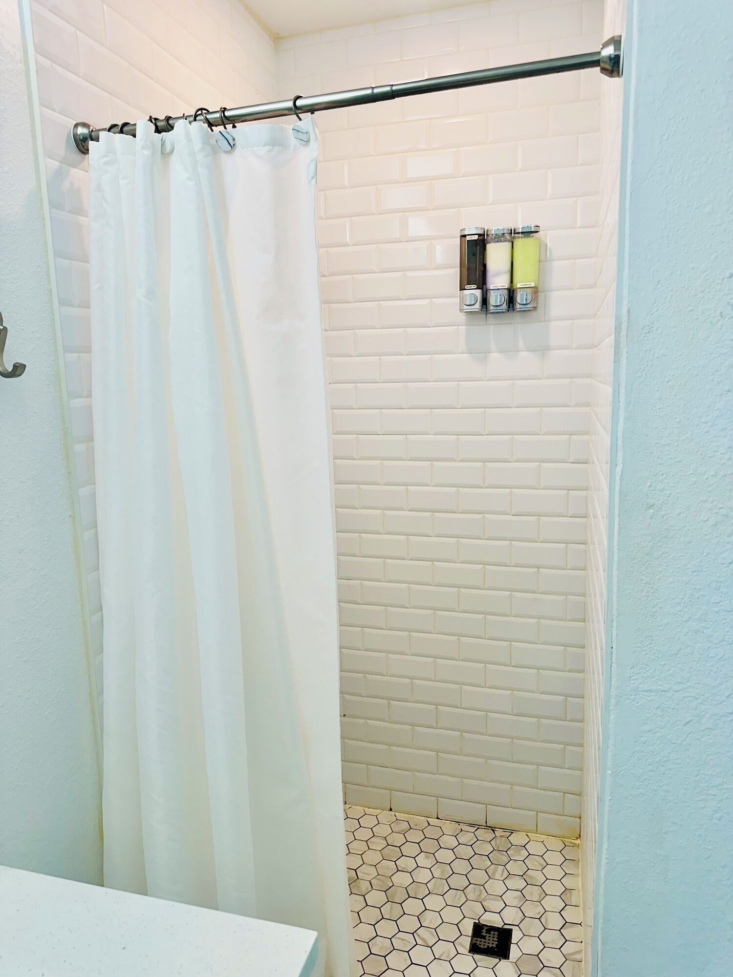 A shower with white tiled walls and a metal curtain rod.