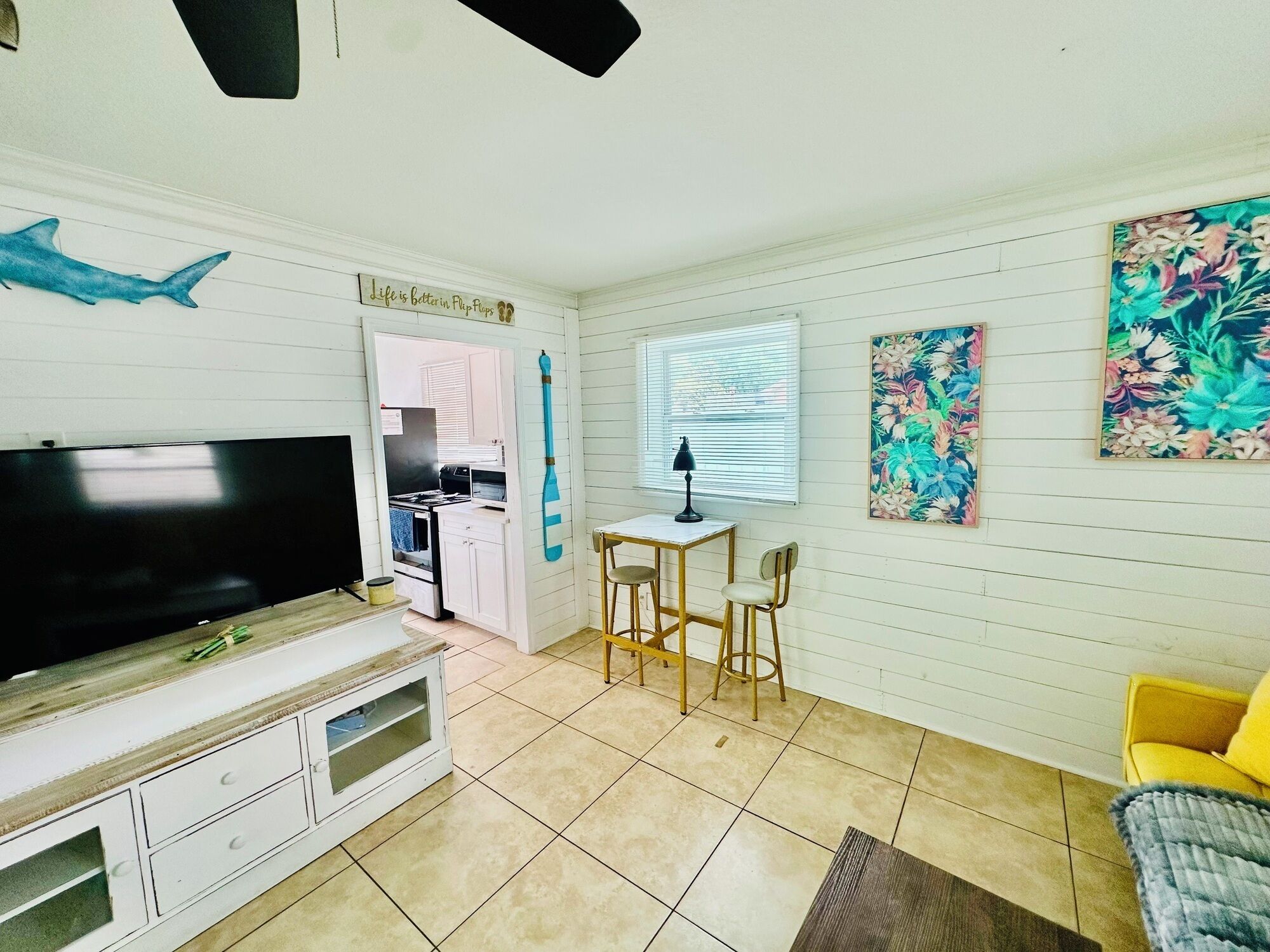 Un espacio habitable compacto con televisor, una mesa de comedor con sillas, una zona de cocina y un sillón amarillo.