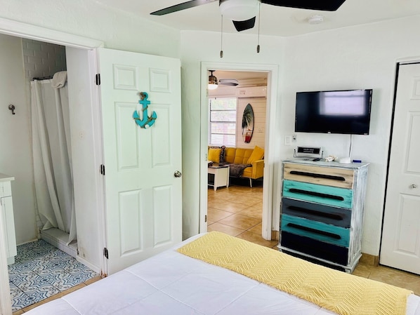 A bedroom with a bed, a television, a dresser, and a bathroom with a shower curtain.