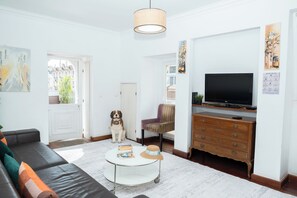 Un salon avec un canapé, une table basse, un téléviseur, un chien et un fauteuil.