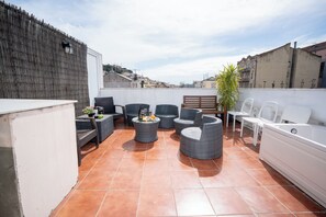 Une terrasse sur le toit, aménagée avec des meubles en osier, un canapé blanc et une petite table sur laquelle sont disposées des boissons.