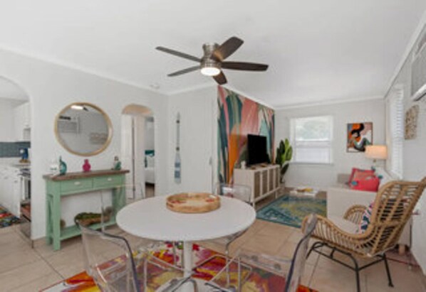 A modern living room with a round table, a ceiling fan, a colorful abstract painting, and a wicker chair.