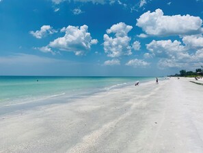 A wide, sandy beach with clear turquoise water and scattered clouds.