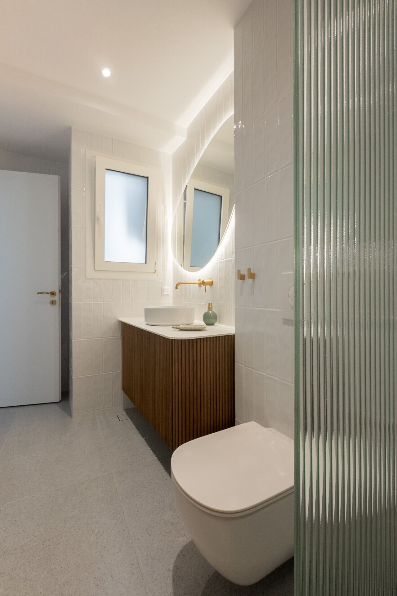 A modern bathroom with a white toilet, a wooden vanity, and a large mirror.